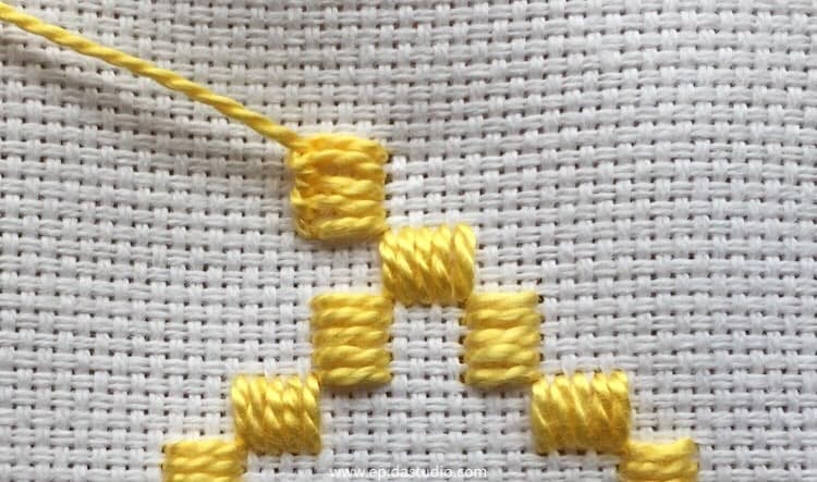 completed blanket stitch unit in hardanger embroidery in yellow thread on white fabric.