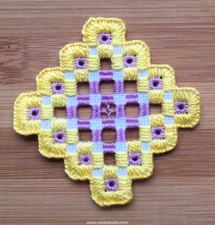 close up of completed hardanger piece embroidered with yellow and purple thread on white fabric.