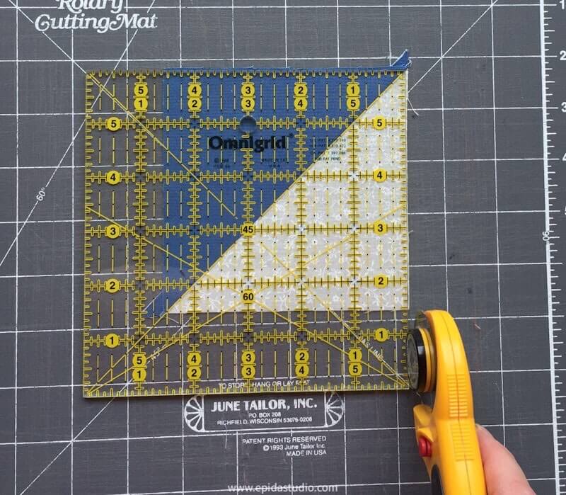 piece of patchwork being trimmed with a quilting ruler and rotary cutter.