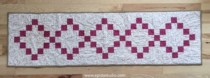 quilted table runner with pink squares in diamond shapes.