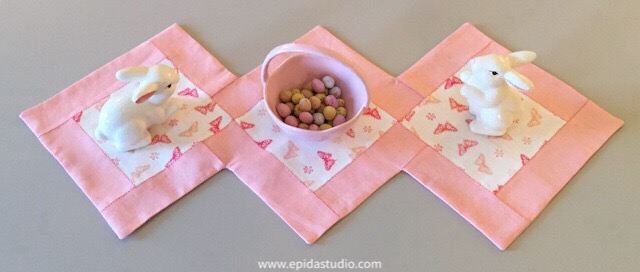 Pink and white table runner with spring decor on it.