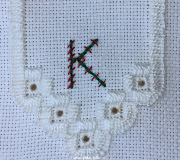 hardanger embroidery in white with a "k" embroidered in red and green cross stitch,