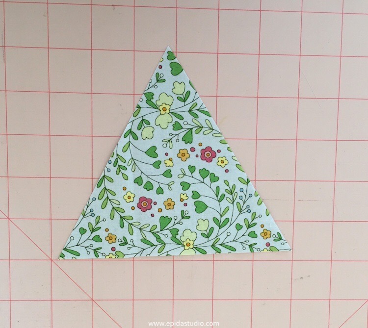 equilateral triangle cut of floral fabric on a pink cutting mat.