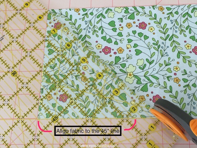 cutting a right angle triangle with a basic quilting ruler and rotary cutter. Floral fabric and pink cutting mat.