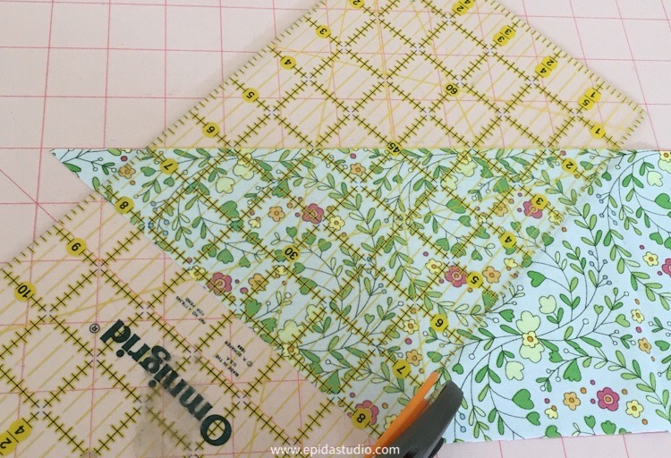 cutting a triangle from a strip of fabric with a rotary cutter and ruler.